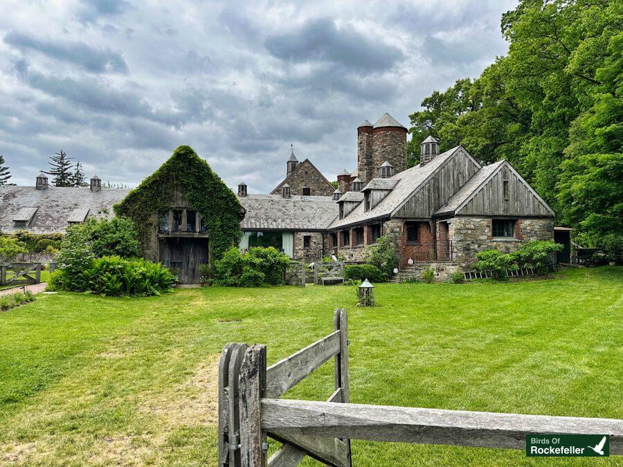 A house with a wooden fence in the middle of a grassy field.