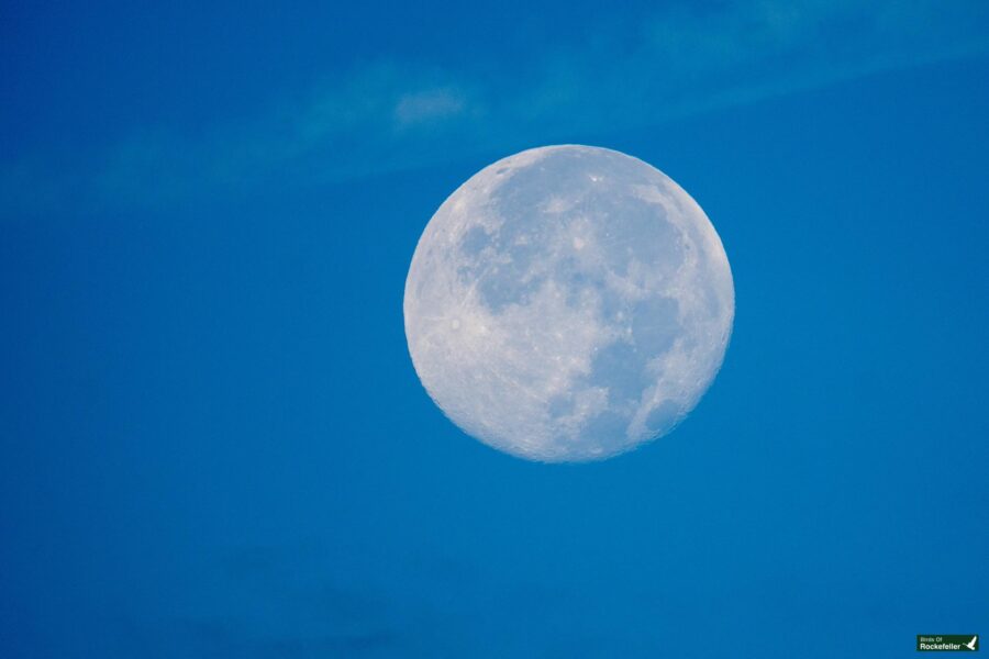 Full moon in a clear blue sky with subtle cloud formations in the background.